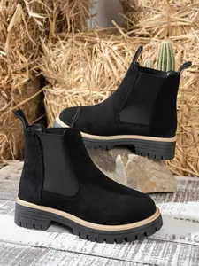 Close-up of black suede Chelsea boots with rugged lug soles on a rustic straw background