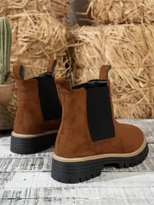 Detail of brown suede Chelsea boots with chunky black lug soles on rustic background