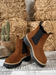Detail view of brown suede Chelsea boots with rugged lug soles on rustic wooden floor.