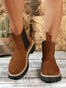 Detailed view of women's brown suede Chelsea boots with thick lug soles in a rustic setting