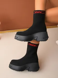 Detailed view of black fly-knit platform sock boots with chunky soles and red cuff accents