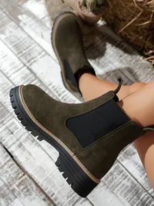 Close-up detail of olive green suede Chelsea boots with chunky black lug sole on wood