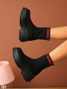 Close-up view of black knit platform sock boots featuring red geometric pattern on cuffs