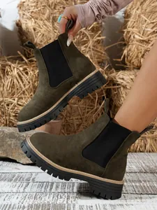 Detailed view of dark green suede Chelsea boots with thick lug soles and side panels