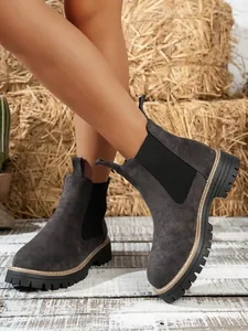 Side view detail of dark grey suede Chelsea boots worn on a model against a rustic background