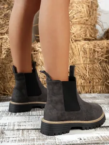 Detailed view of grey suede Chelsea boots with thick non-slip soles on rustic straw background