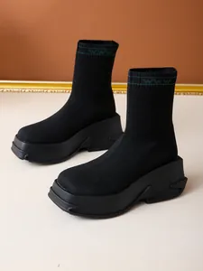 Close-up side view of black knit platform sock boots featuring decorative green collar patterns.