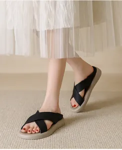Detail view of black criss-cross strap flat sandals on model's feet with white skirt