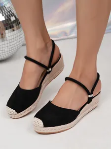 Close-up van zwarte espadrilles met sleehak, gevlochten touwzool en enkelbandje