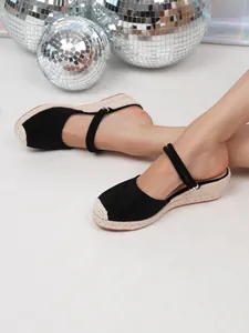 Detailopname van zwarte sleehak-espadrilles voor dames met geweven zool en bandjes.