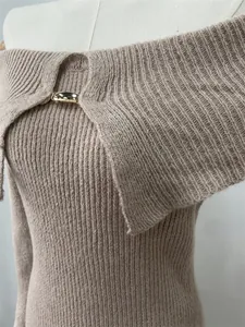 Close-up of elegant off-shoulder knitted dress with gold metal buckle detail.
