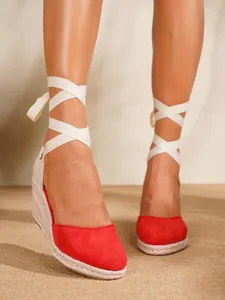 Detalle de sandalias de cuña tipo alpargata rojas con cintas blancas atadas al tobillo