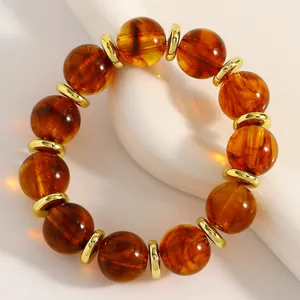 Detailansicht von bernsteinfarbenen Perlen mit goldenen Metall-Abstandshaltern an einem Armband.