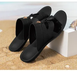 Détail des sandales noires pour hommes avec emblème doré sur une plage de sable.