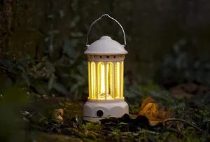 Retro style white portable camping lantern glowing with warm yellow LED light outdoors