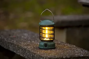 Vintage army green outdoor camping lantern emitting warm LED light on a natural stone surface.