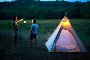 Due uomini che campeggiano di notte con una lanterna LED vintage vicino a una tenda tepee.