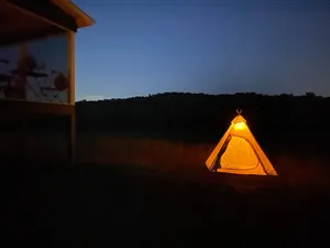 Luce da campeggio a LED calda che illumina una tenda tipi in un sereno paesaggio notturno.