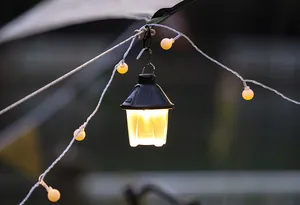 Portable LED pinecone camping lantern with warm yellow light hanging in a tent site