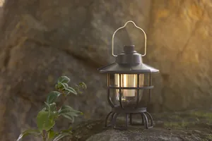 Vintage portable outdoor camping lantern glowing on rocks in soft warm light