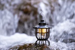Detailed view of a retro waterproof rechargeable camping lantern on wet rock by a waterfall