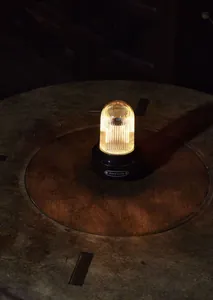 Detailed close-up of a retro rechargeable LED camping lantern glowing on a dark wooden table