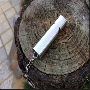 Close-up of a high-frequency aluminum alloy survival whistle on a rustic wood stump.