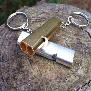 Detail of gold and silver aluminum dual-tube survival whistles on a wooden stump