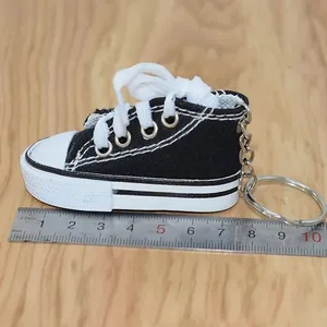 Detailed side view of a black miniature canvas shoe keychain with ruler for size.