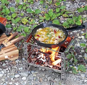 Dettaglio di una stufa a legna portatile in acciaio inox accesa in un campeggio all'aperto.