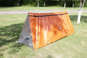 Detailed view of an orange and silver PE emergency thermal tent set up on grass.