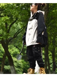 Model holding a portable multi-functional camping entrenching tool in a lush forest