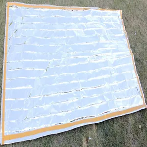 Detailed view of silver thermal emergency blanket with orange border on grass.