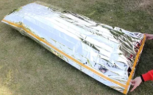 Emergency survival sleeping bag made of silver PET aluminum film on outdoor grass.