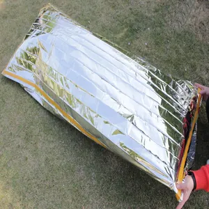 Silver PET aluminum film emergency sleeping bag spread out on green grass outdoors