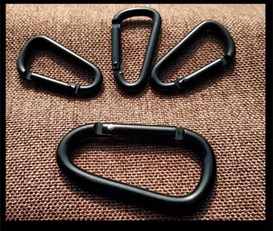 Close-up detail of four matte black aluminum D-shaped carabiners on brown fabric
