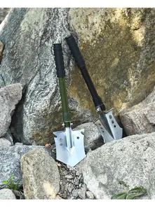 Close-up detail of green and black folding multi-functional tactical shovels on rocks