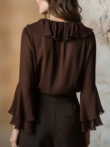 Vista trasera de blusa marrón de manga larga con cuello de volantes y mangas acampanadas.