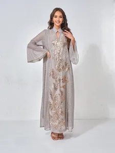 Détail d'une robe longue grise avec broderie de paillettes dorées et manches évasées.