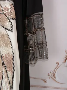 Détail d'une robe ethnique avec broderies de perles dorées et noires sur manches en tulle fin.