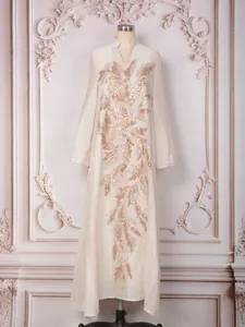 Close-up of elegant ivory kaftan dress with intricate gold sequin leaf embroidery details