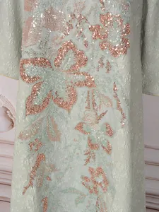 Gros plan d'une robe longue à paillettes avec des motifs floraux or rose sur tissu vert.