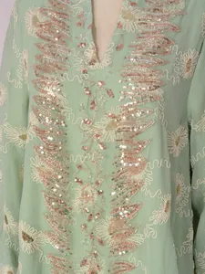 Primo piano del ricamo intricato di paillettes e perline su un abito in rete verde chiaro.
