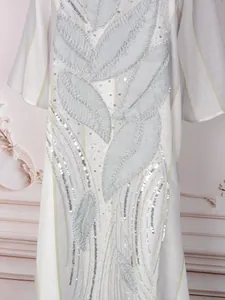 Dettaglio di un elegante abito bianco con paillettes e ricami a forma di foglia.