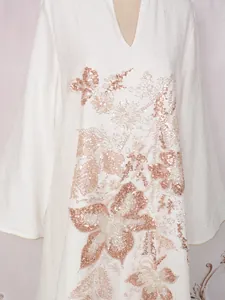 Gros plan d'une robe longue blanche avec broderies florales en paillettes or rose