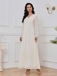 Mannequin portant une robe longue blanche à pois dorés dans un décor de studio élégant