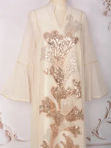 Détail d'une robe beige de luxe avec broderie florale en paillettes dorées et manches cloche.