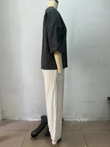 Seitenansicht eines zweiteiligen Damen-Sets mit dunklem Top und weißer Hose.