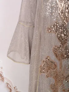 Gros plan sur la broderie de paillettes dorées et la manche cloche d'une robe de luxe