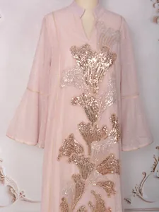 Détail d'une robe rose avec une broderie de paillettes dorées et un col mao élégant.